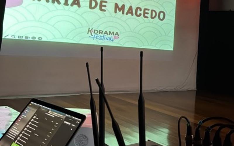 Sonorização para eventos em São Paulo: antenas de microfone sem fio ao lado da mesa de som, com o palco ao fundo